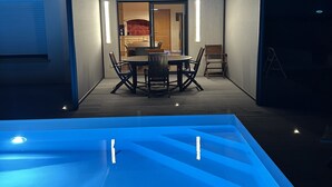 Ein moderner Essbereich im Freien mit Pool, einer überdachten Terrasse und einer durch Glastüren einsehbarer Küche.