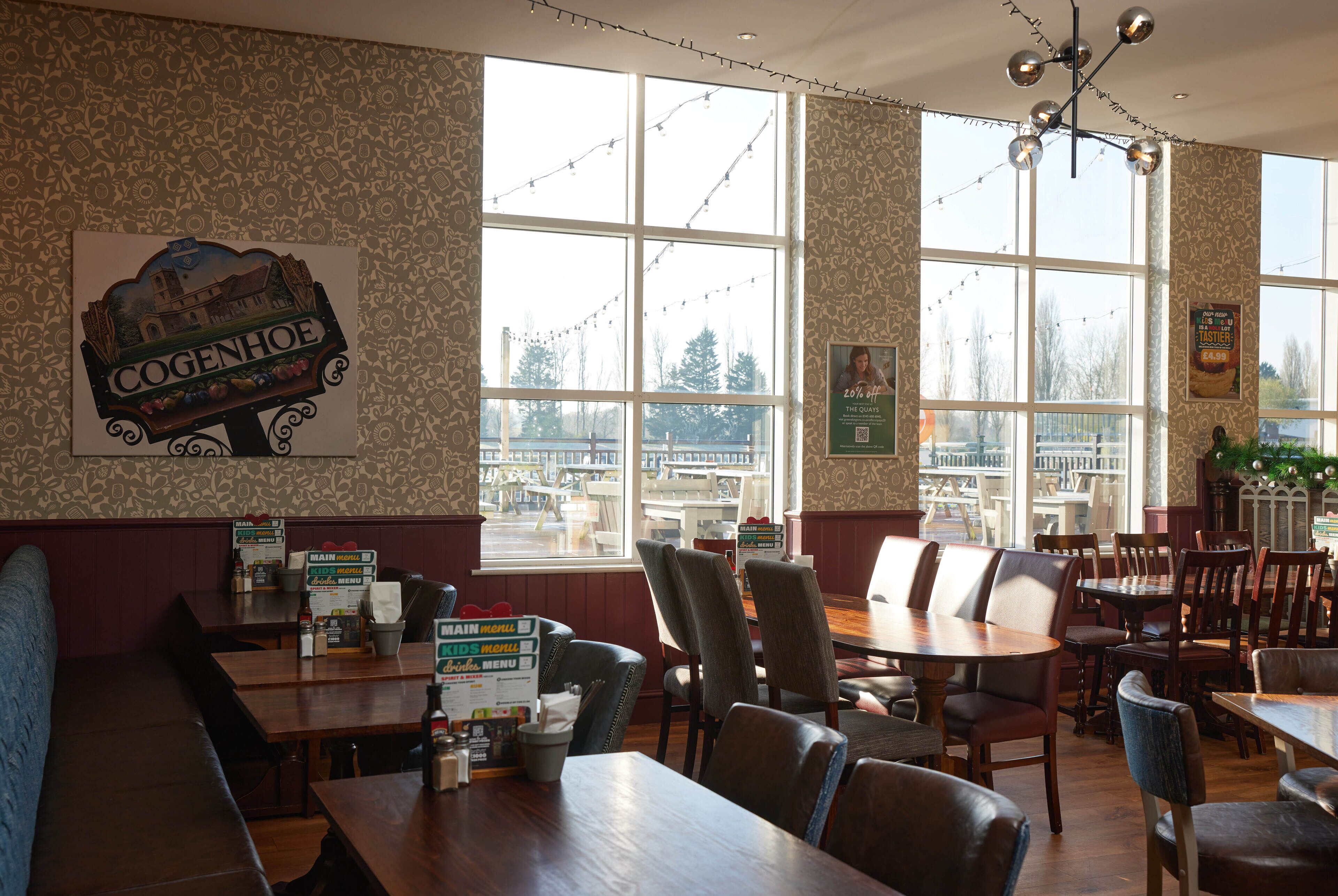 A restaurant interior with wooden tables and chairs, a large window with a view, and a sign on the wall.