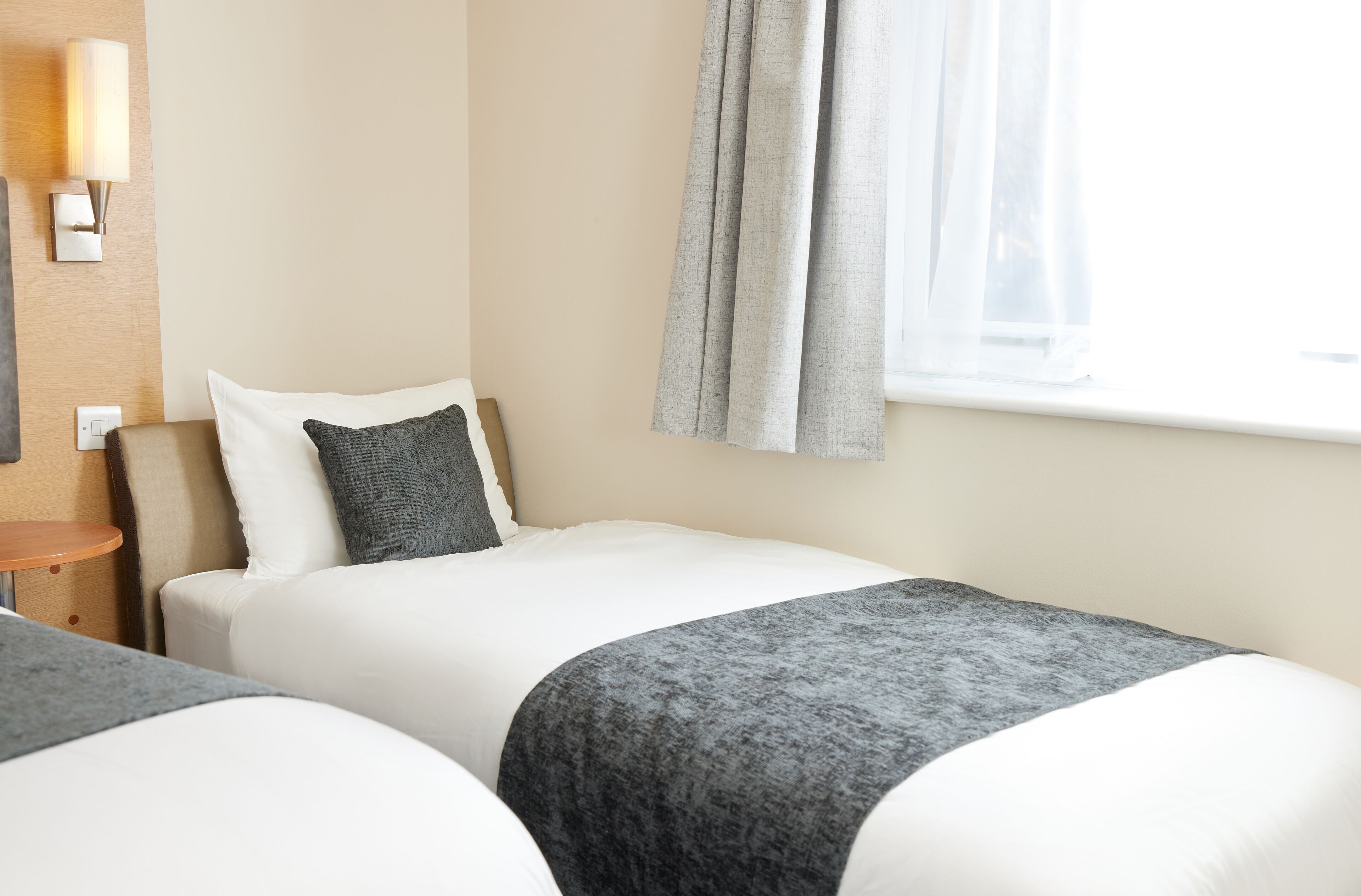 Une chambre d’hôtel avec deux lits, une table de chevet, une lampe et une fenêtre avec des rideaux.