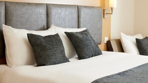 A neatly made bed with white and dark gray pillows, a gray headboard, and a wall-mounted light fixture. - The Quays By Greene King Inns (Northampton)