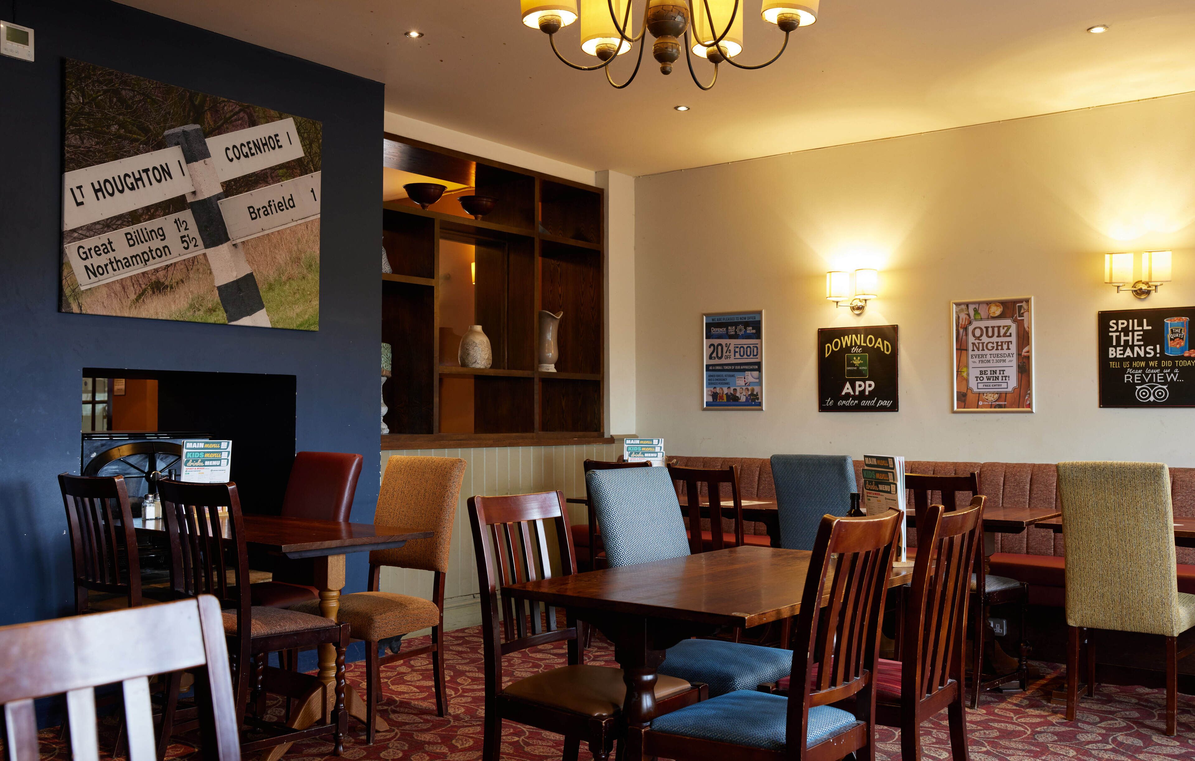 A restaurant with wooden tables and chairs, a chandelier, and wall decorations including a sign with directions and posters.