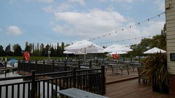 An outdoor patio area with wooden tables and benches, string lights, and umbrellas.