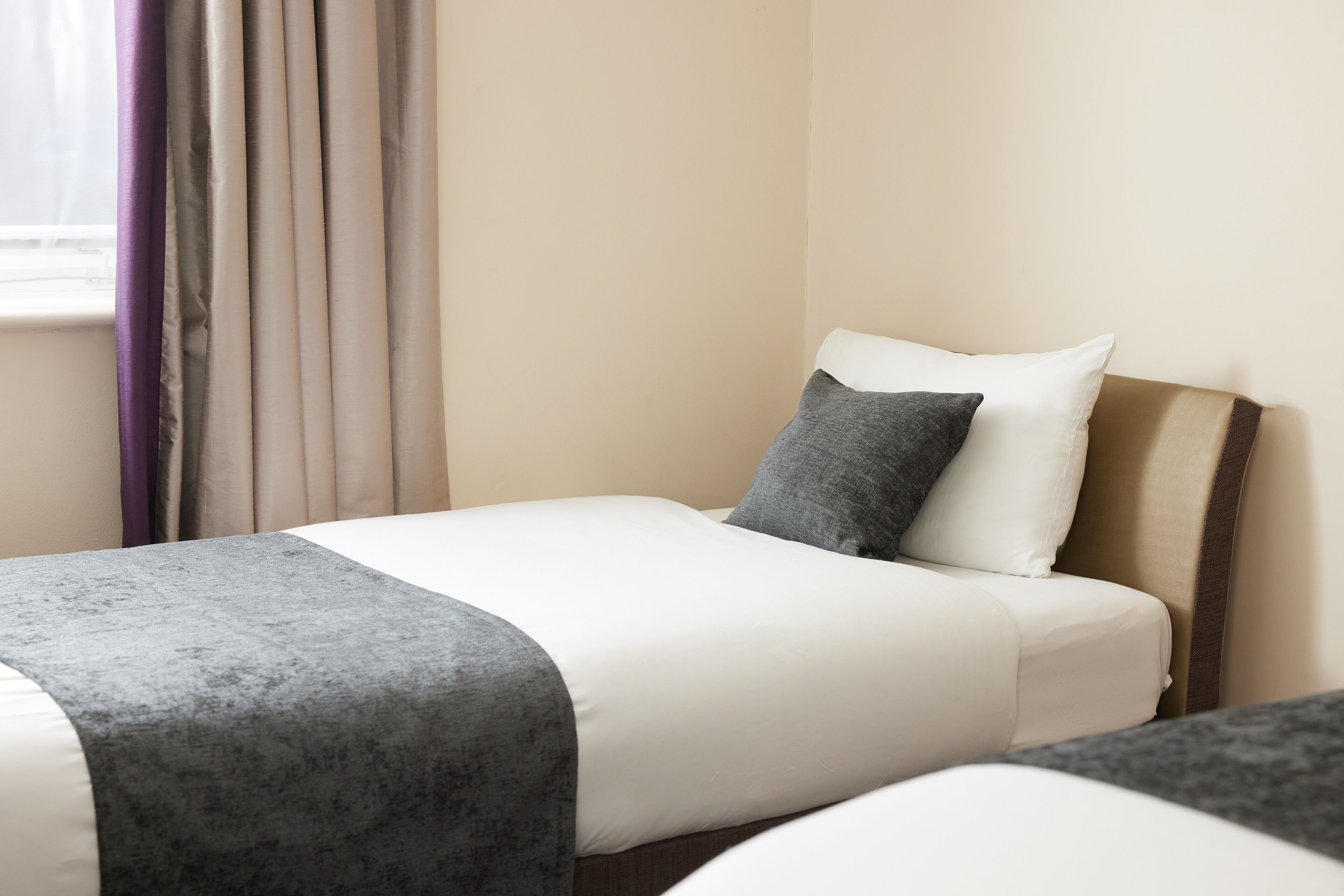 Ein Hotelzimmer mit einem Bett, einem Fenster mit Vorhängen und einem Kopfteil.