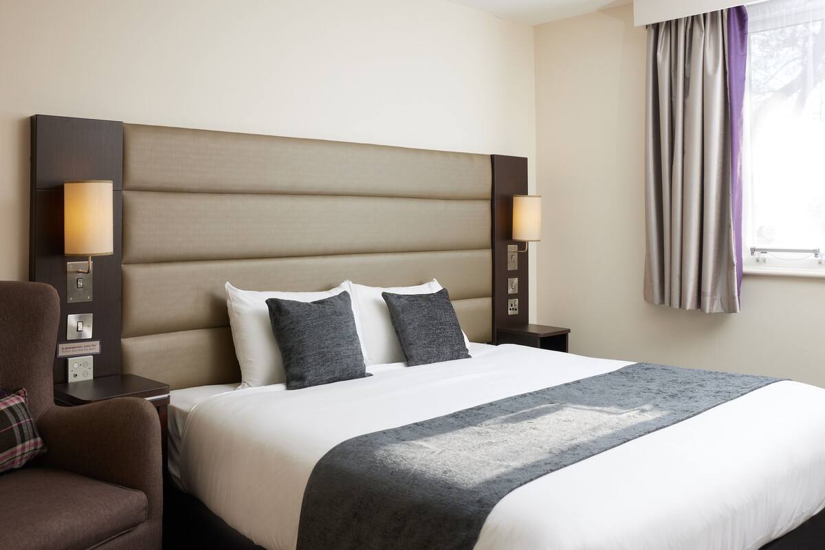 A hotel room with a large bed, two bedside lamps, a chair, and a window with curtains.