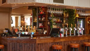 A bar area with multiple beer taps, a cash register, and stools. - The Quays By Greene King Inns (Northampton)