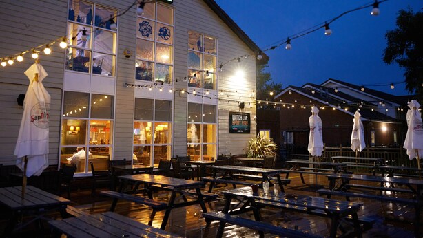 A pub with outdoor seating, string lights, and a sign indicating a watch live sport area. - The Quays By Greene King Inns (Northampton)
