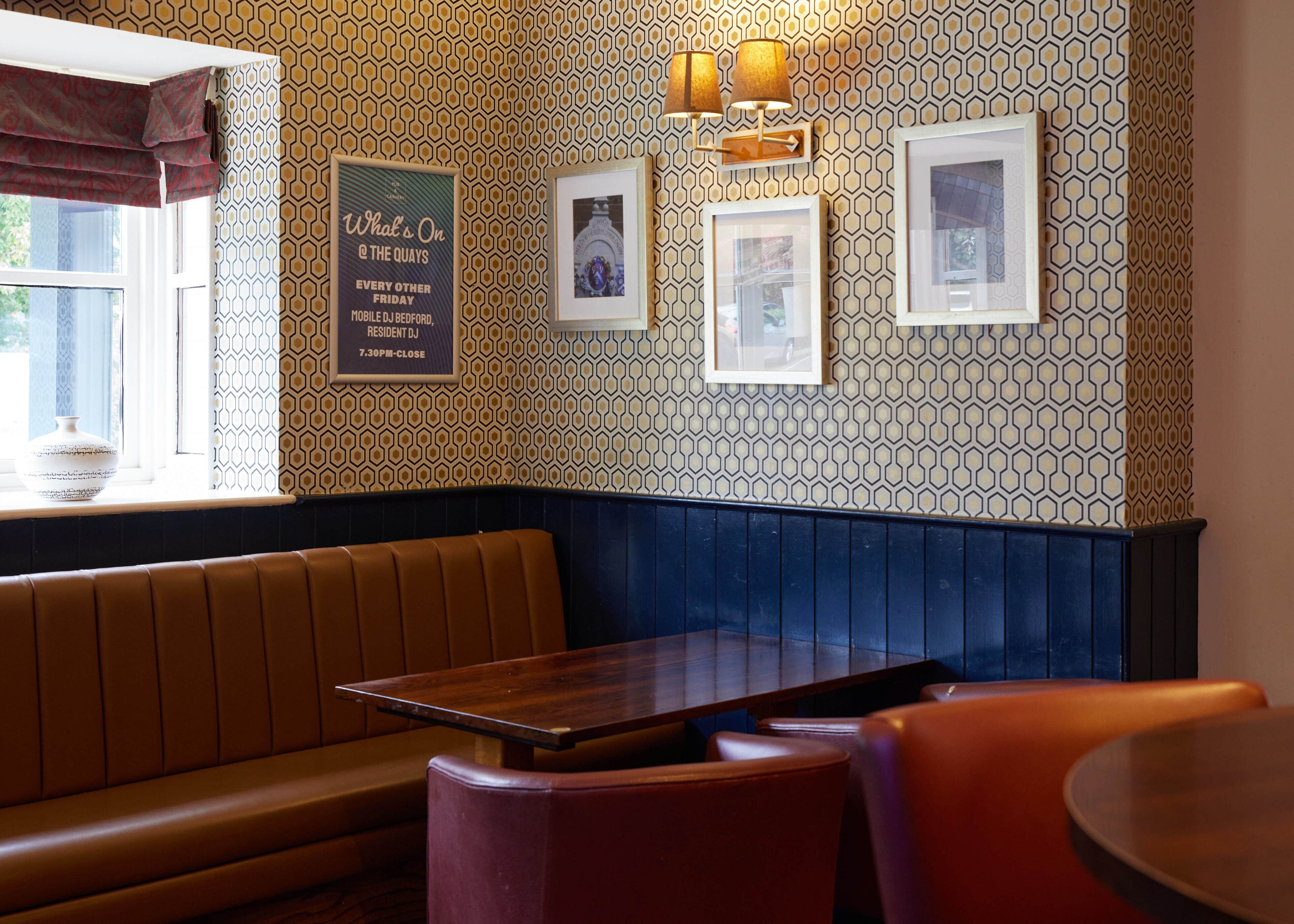 A restaurant interior with a patterned wall, a wooden table, and a booth seating area.