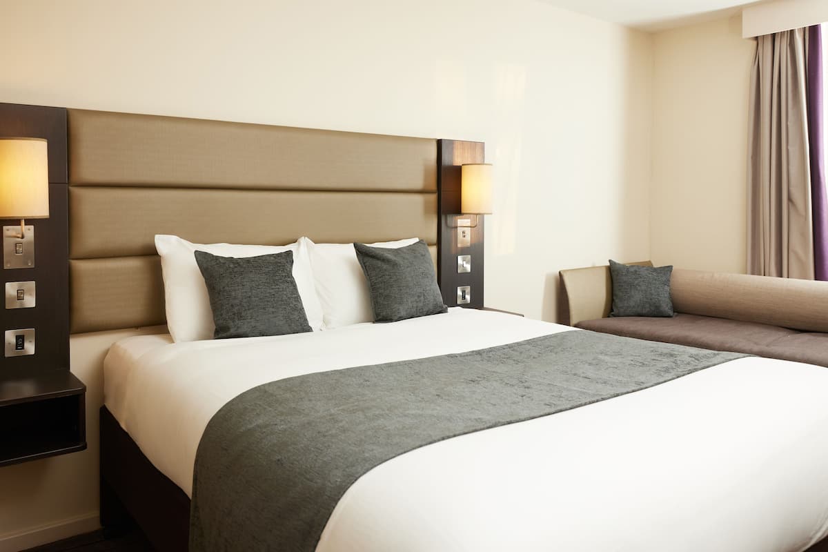 A hotel room with a large bed, a sofa, and a nightstand with a lamp.