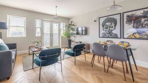 A modern living room with a dining area, large windows, a flat-screen TV, and artwork on the wall. - Modern 2 Bed Oasis -Parking & Garden - By Tempstay (Berkshire)