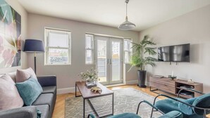 A living room with a sofa, chairs, a coffee table, a TV, and a large plant. - Modern 2 Bed Oasis -Parking & Garden - By Tempstay (Berkshire)