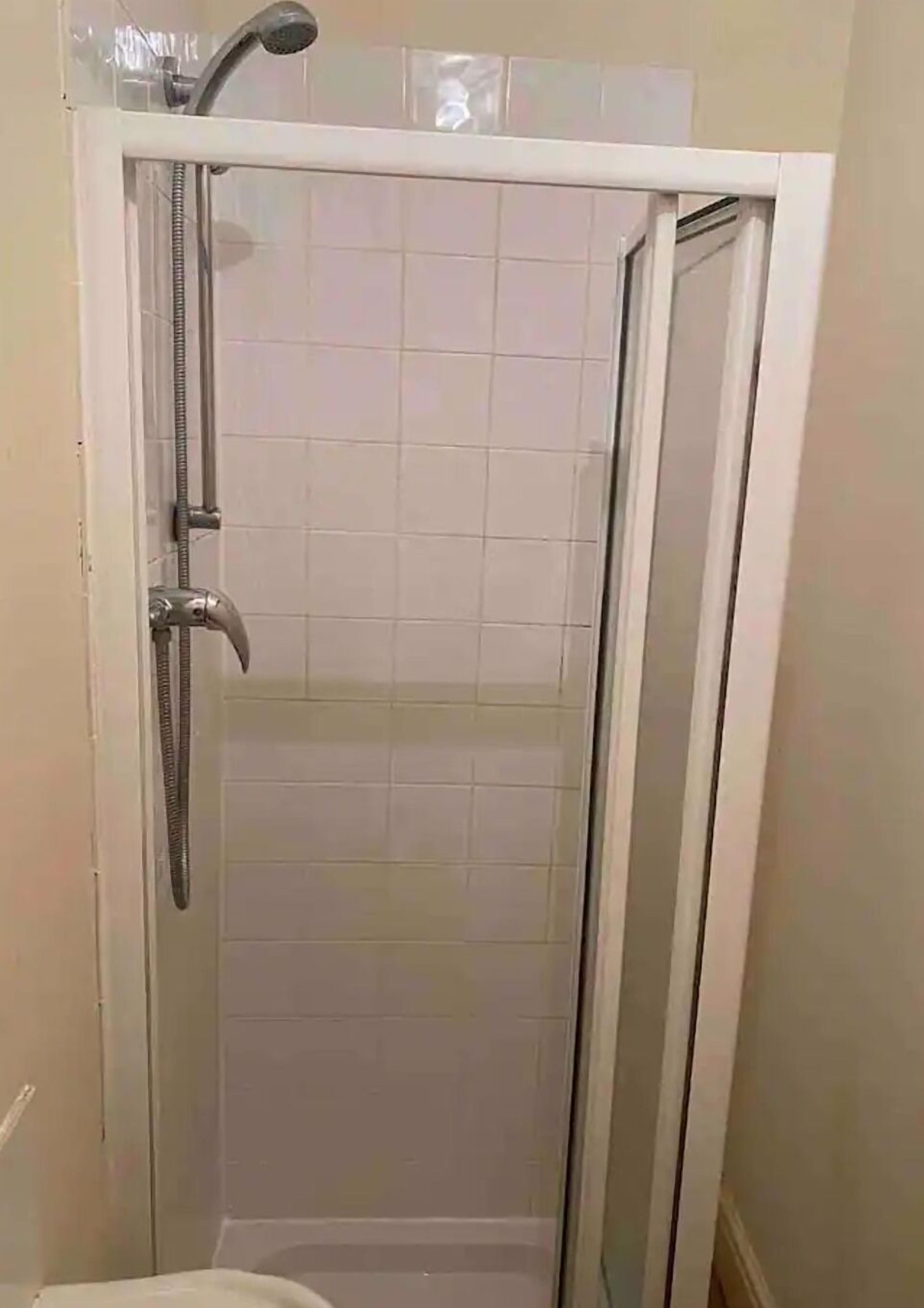 A glass-enclosed shower stall with a handheld showerhead and a wall-mounted faucet.