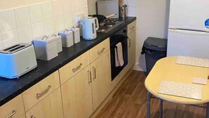 A compact kitchen with wooden cabinets, a countertop with a toaster, kettle, and other appliances, a small table, and a refrigerator. - Flat 3, 52 Sneinton Hermitage Nottingham NG2 4BS (Nottingham)