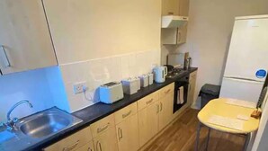 A compact kitchen with wooden cabinets, a built-in washing machine, a sink, and a small dining table. - Flat 3, 52 Sneinton Hermitage Nottingham NG2 4BS (Nottingham)