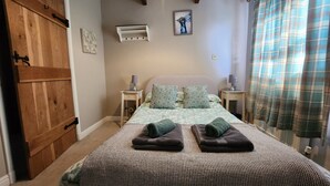Une chambre à coucher avec un lit, deux tables de chevet, une porte en bois, un appareil de climatisation, un tableau et un rideau à carreaux.