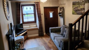Un salon chaleureux avec un plancher en bois, un canapé, un téléviseur et une fenêtre avec des rideaux.