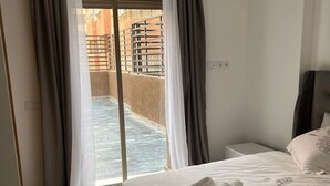 A hotel room with a bed, a nightstand, and a view of a pool area through a sliding door. - 1bed Apartment - Sleeps 4 - Balcony, Wifi, Parking (Marrakech)
