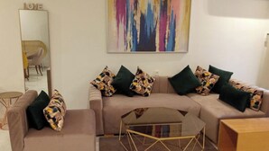 A living room with a sofa, a matching armchair, a coffee table, and a mirror on the wall. - 1bed Apartment - Sleeps 4 - Balcony, Wifi, Parking (Marrakech)