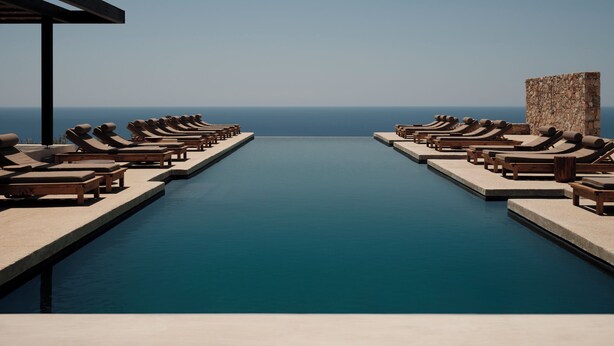 A poolside area with lounge chairs and a stone wall, overlooking the sea. - Gundari (Folegandros)