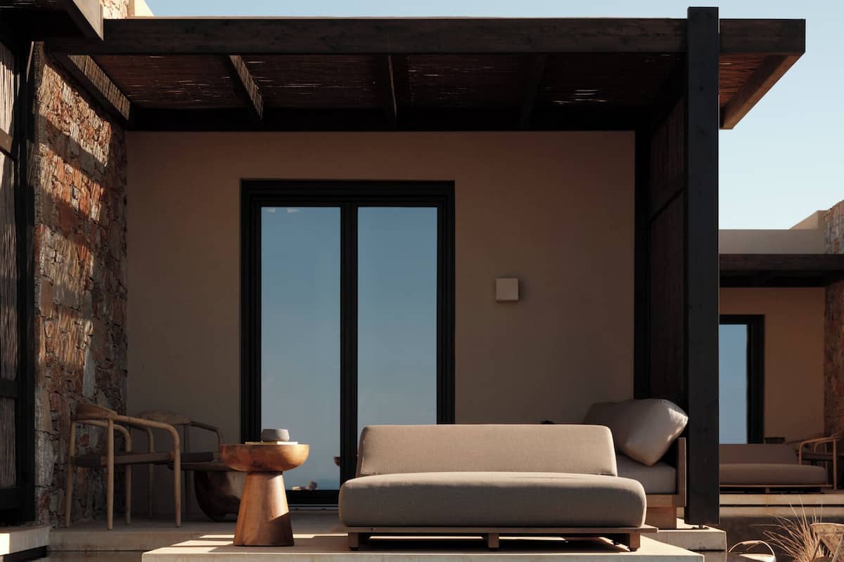 A modern outdoor seating area with a sofa and chairs, a stone wall, and a pool.