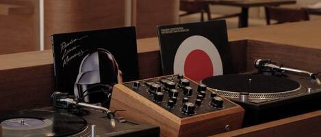 A wooden DJ booth with turntables and audio equipment, a black sign with white text, and a red and white circular design.