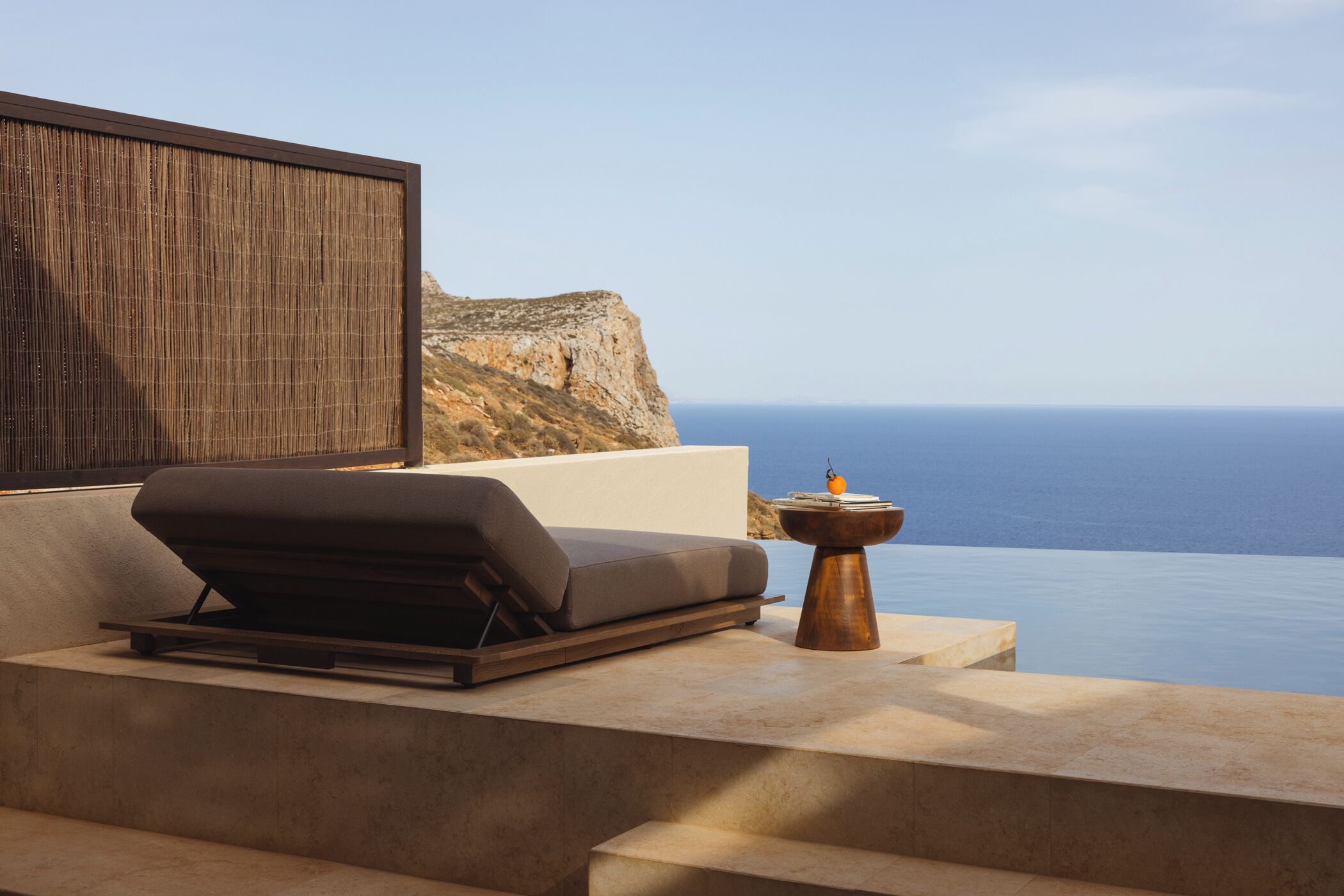 A modern outdoor seating area with a view of the sea and a cliff.