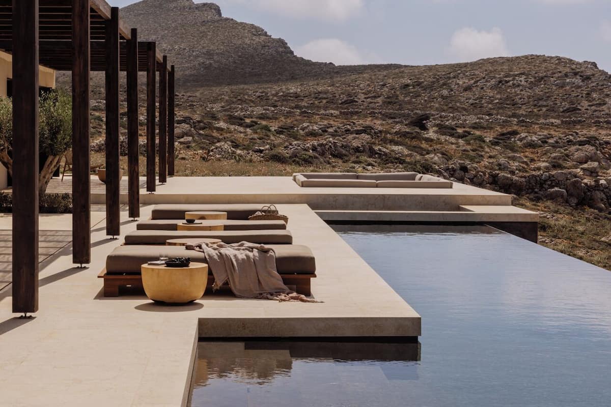 A poolside area with lounge chairs and a pergola, overlooking a mountainous landscape.