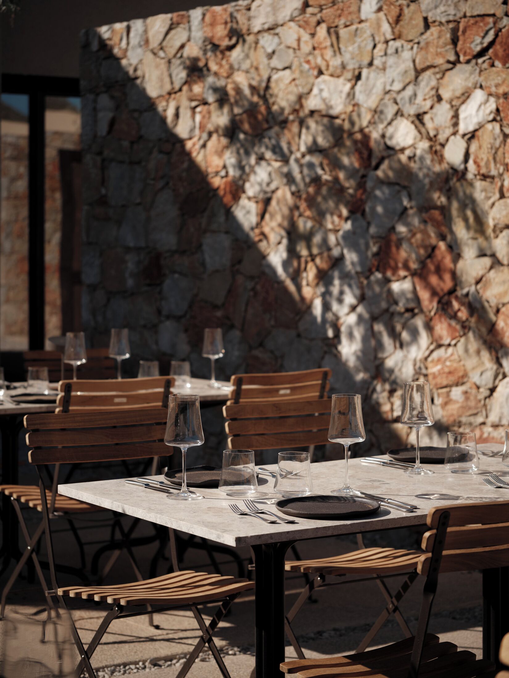 An outdoor dining area with stone walls, wooden tables, and chairs.