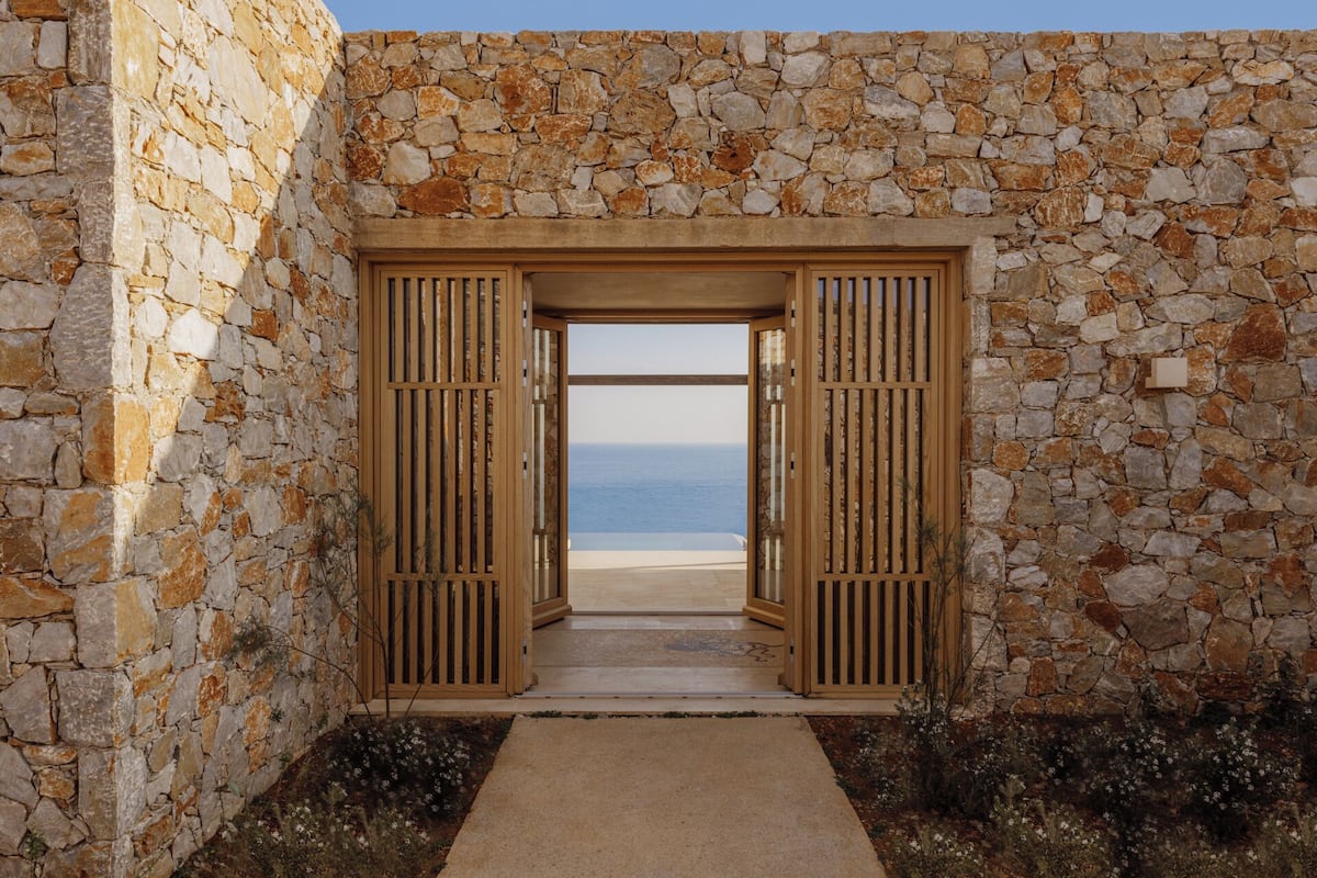 A stone wall with a wooden door leading to a beach view.