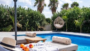 A poolside lounge area with a sun lounger, a hanging chair, and a table with a towel and fruit.