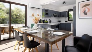 A modern kitchen with dark cabinets, a central island, and a dining area with a glass table and chairs.