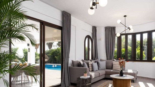 A modern living room with a grey sofa, a coffee table, and a pool view.