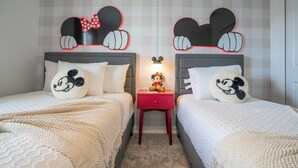 A bedroom with two beds, each with a Mickey Mouse themed headboard, a small red nightstand, and a Mickey Mouse plush toy.