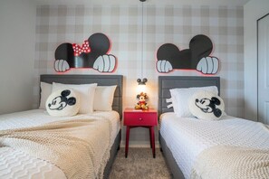 A bedroom with two beds, each with a Mickey Mouse themed headboard, a small red nightstand, and a Mickey Mouse plush toy.