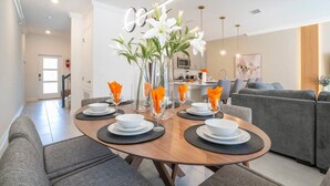 A modern dining area with a round table set for four, surrounded by grey sofas. - Magnificient 4Bd w/ Pool @ Storey Lake Resort 2648 (Kissimmee)