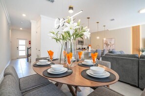 A modern dining area with a wooden table set for four, surrounded by grey sofas. - Magnificient 4Bd w/ Pool @ Storey Lake Resort 2648 (Kissimmee)