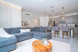 A modern living room with a grey sectional sofa, a wooden coffee table, and a kitchen area with grey cabinets and a microwave.
