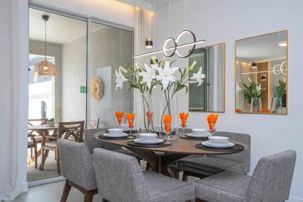 Un comedor moderno con una mesa redonda, sillas tapizadas en gris y un jarrón con flores blancas.
