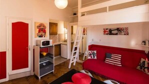 Une pièce compacte avec un canapé rouge, un petit coin cuisine et un espace en mezzanine.