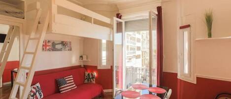 A room with a red sofa, a glass table with chairs, a ladder, and a window with curtains.
