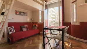 Une pièce chaleureuse avec un canapé rouge, une table à manger entourée de chaises et une fenêtre agrémentée de rideaux.