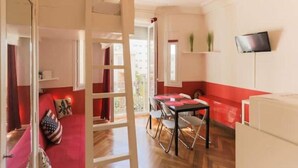 Une pièce comprenant une table à manger, des chaises, un téléviseur fixé au mur, et une décoration aux couleurs rouge et blanche.