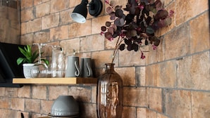 A kitchen with a brick wall, a wooden shelf with kitchenware, and a vase with flowers. - Cathedral Superior Apartment (Worcester)