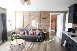 A modern living room with a sofa, coffee table, and a brick wall. - Cathedral Superior Apartment (Worcester)