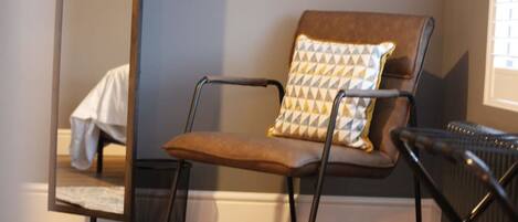 A modern chair with a geometric pillow, a radiator, and a mirror reflecting part of the room.