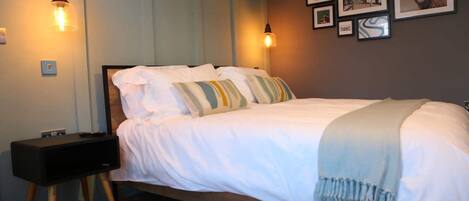 A neatly made bed with white linens and striped pillows, a bedside table with a lamp, and framed artwork on the wall.