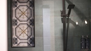 A shower area with a patterned tile wall, a handheld showerhead, and two bottles of shampoo. - Diglis Basin Apartment (Worcester)