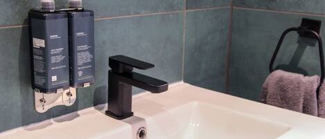 Un baño con un lavamanos blanco, grifo negro y dos dispensadores negros en la pared.