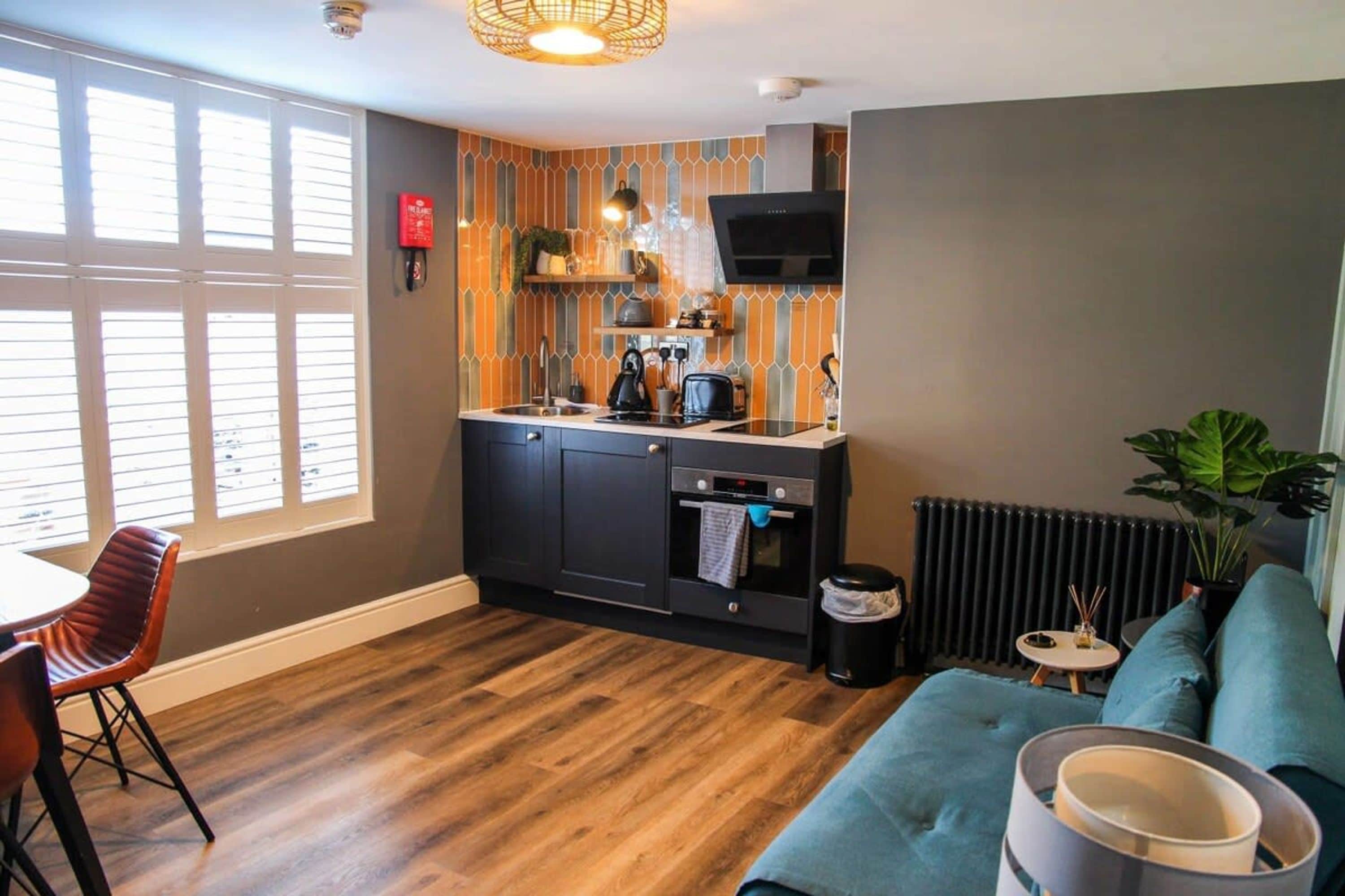 A compact kitchen with a built-in oven, a dining area with a table and chairs, and a cozy seating area with a sofa and a plant.