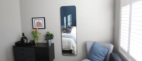 A bedroom with a bed, a dresser, a mirror, a radiator, and a window with blinds.