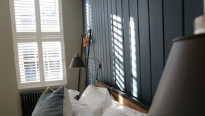 A bedroom with a bed, a nightstand, a lamp, and a window with blinds. - Hop Market - Ensuite Bedroom (Worcester)